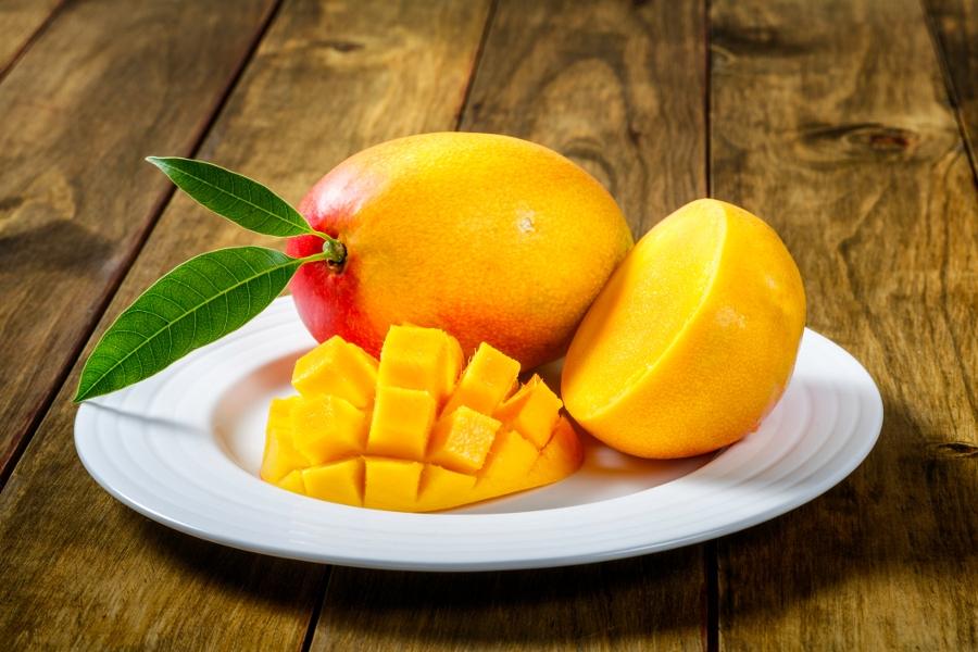 Tropical fruits   Sliced Mango on a plate ready for breakfast. All set over a wooden table. The mango belongs to the genus Mangifera and to the flowering plant family Anacardiaceae.  The mango is a juicy stone fruit and is native to south and southeast As