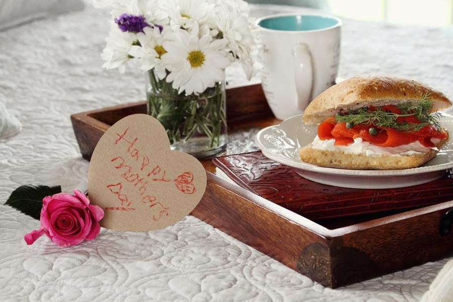Child's handwriten message on heart shaped card and flowers with breakfast served in bed. Extreme shallow depth of field with selective focus on heart.